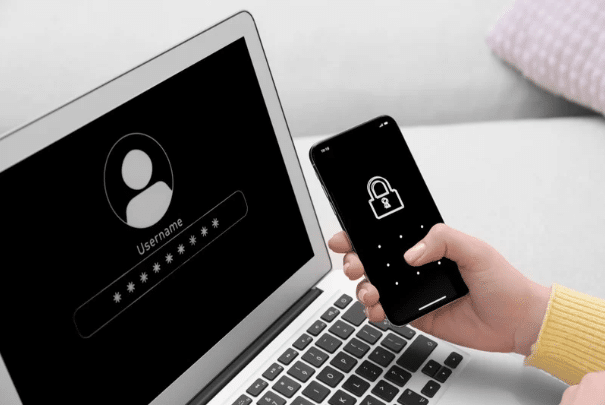 A person securely holds a smartphone with a lock screen beside a laptop displaying a login page, emphasizing the importance of cybersecurity.