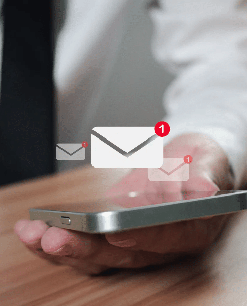 A person holds a smartphone, featuring floating email icons with notification badges displaying the number one, likely indicating messages sent to a professional email address.