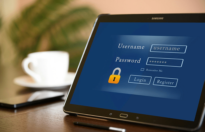 Tablet displaying a login screen with fields for username and password, featuring a yellow lock icon. A "Remember Me" checkbox is shown above the login and register buttons.