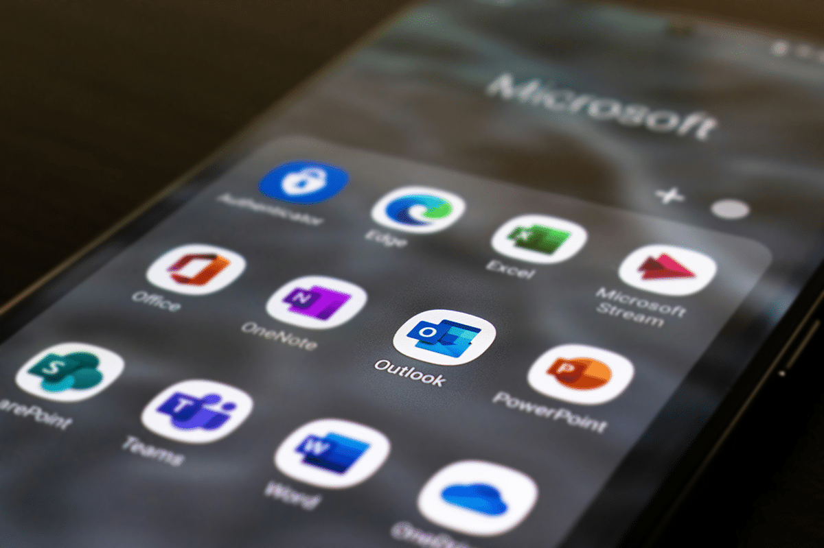 A smartphone screen showcases Microsoft apps, such as Outlook, where you can effortlessly set up email, alongside Teams, Word, Excel, PowerPoint, OneNote, Stream, and Edge.