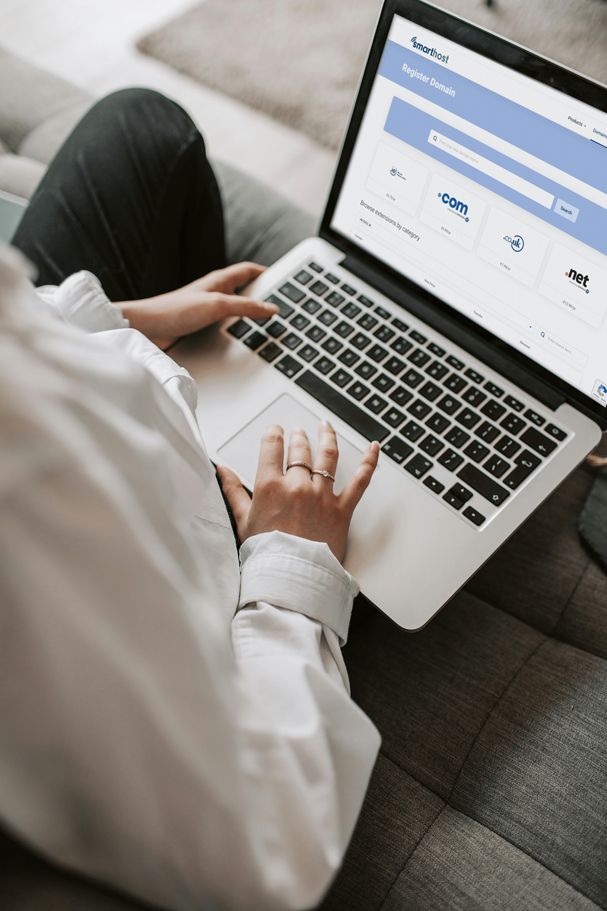 A person in a white shirt sits on a couch, using a laptop displaying an IE domain registration website.