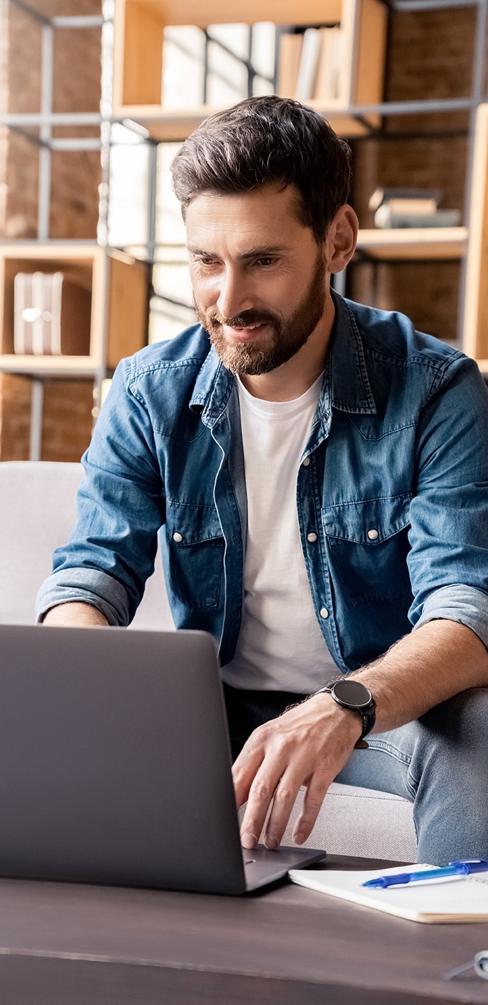 A man in a denim jacket, utilizing Professional Email Services with SmartHost, is working on a laptop in a modern office space.