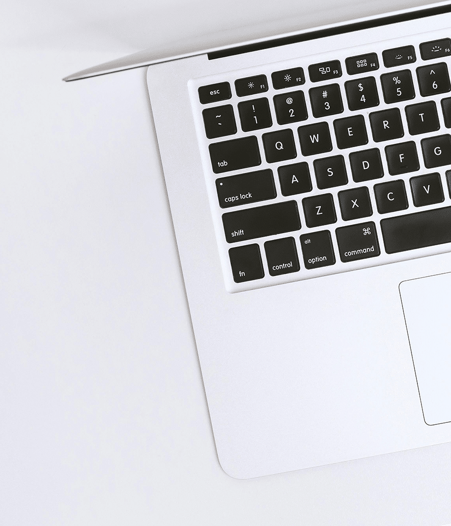 A partial view of a silver laptop keyboard and trackpad on a white surface, photographed from above.