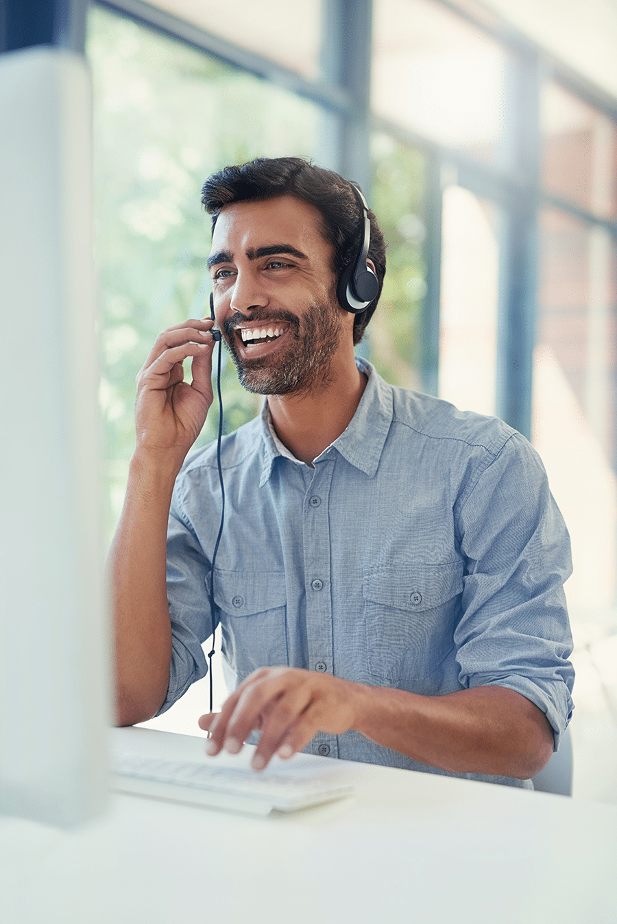 A man wearing a headset is smiling and looking at a computer screen while typing on a keyboard.