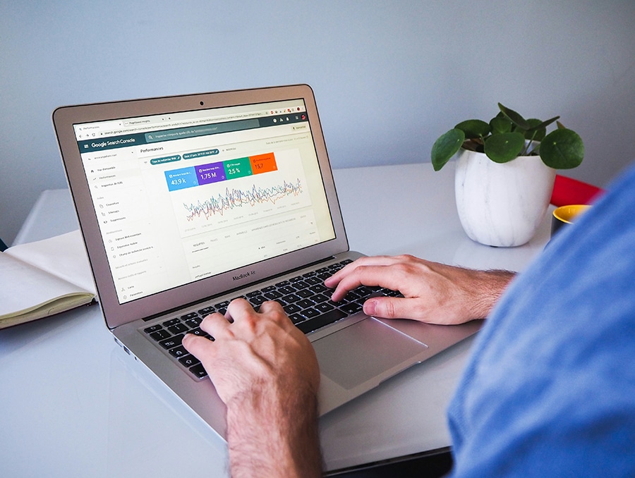 Person typing on a laptop viewing Google Search Console analytics, with a plant and notebook in the background.