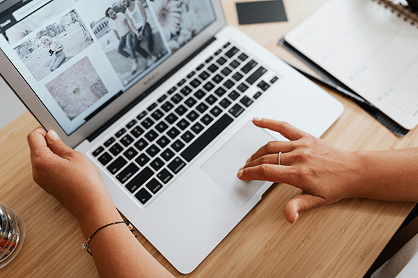 A person uses a laptop, viewing a webpage displaying several photos, with one hand on the keyboard and the other on the trackpad.