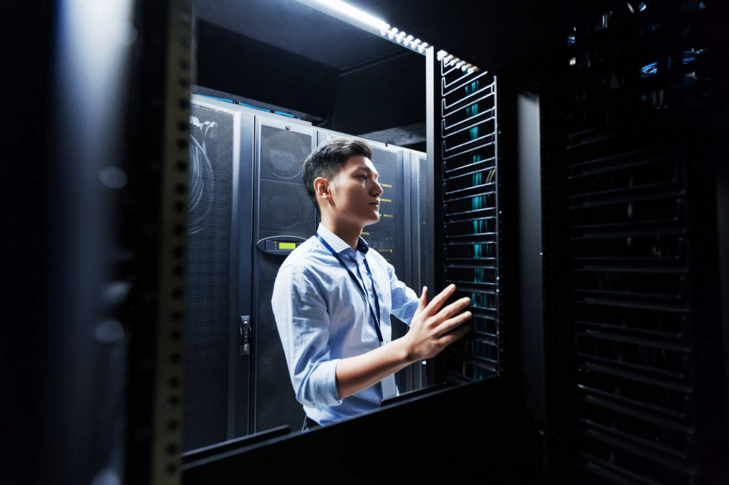 A person in business attire is working with server racks in a data center, inspecting or configuring equipment.